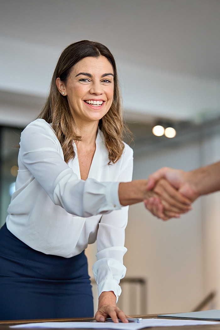 Freundliche Geschäftsfrau begrüßt Kunden mit Handschlag und schafft Vertrauen